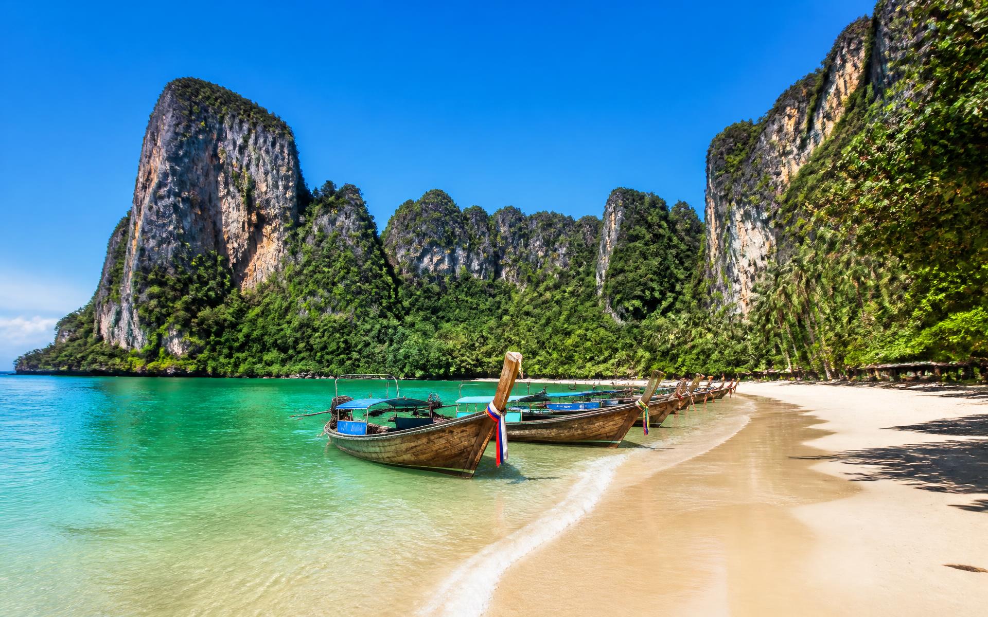 towering limestone cliffs above a turquoise bay with longtail boats at Krabi & Railay, Thailand — original Triple VIP destination visual.