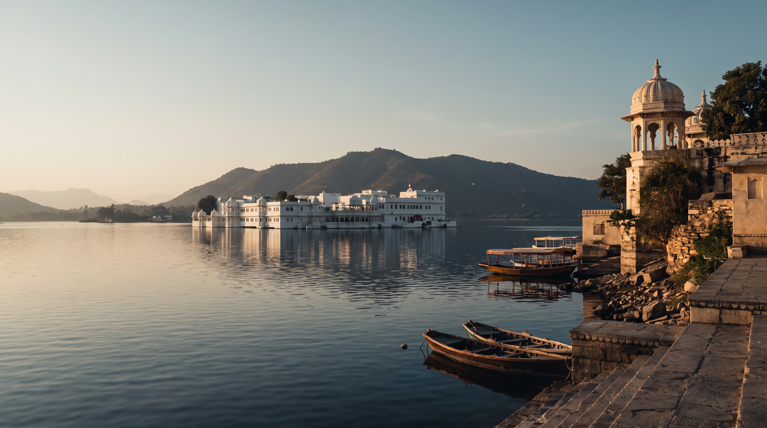 white marble palaces on Lake Pichola with the Aravalli hills behind at Udaipur, India, in sunset light — original Triple VIP destination visual.