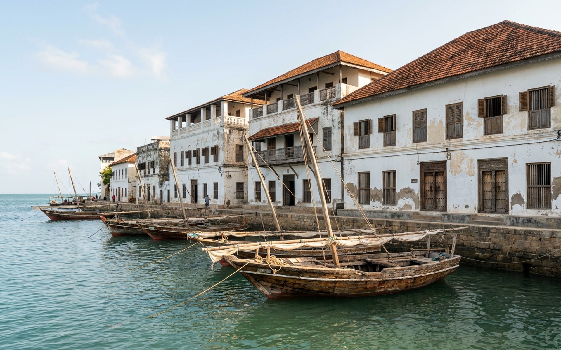 carved wooden dhows on a channel before whitewashed coral-stone houses with a stone waterfront at Lamu, Kenya — original Triple VIP destination visual.