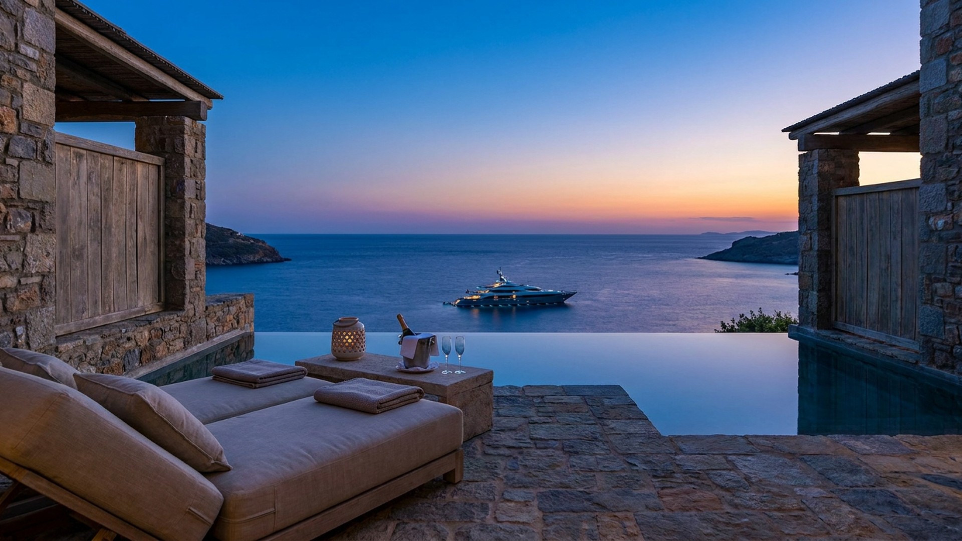 Private infinity terrace at blue hour above a calm bay with a distant yacht