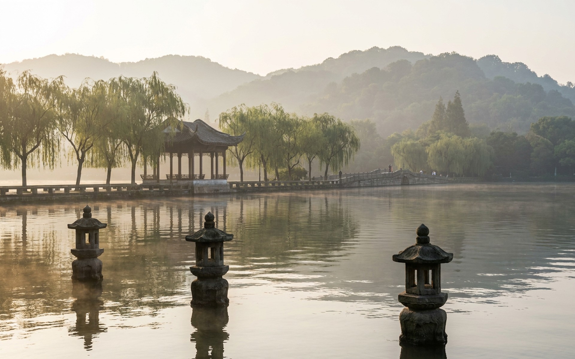 Dawn mist over West Lake in Hangzhou with the stone lanterns of Three Pools Mirroring the Moon, willow causeway and wooded hills