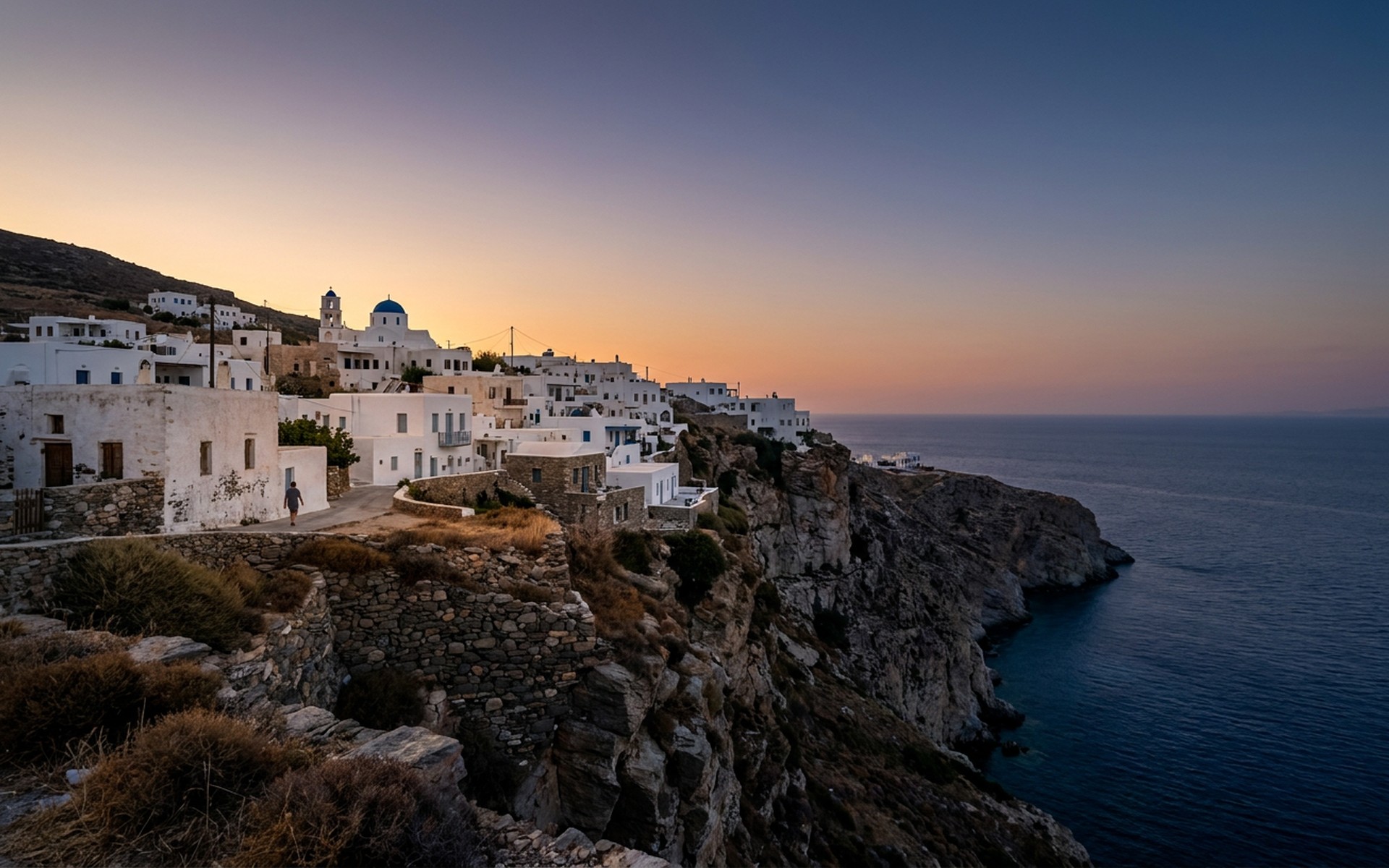 The traditional Chora village of Folegandros with its whitewashed houses and blue-domed church, clinging to a dramatic cliffside overlooking the Aegean Sea at dusk. at Folegandros, Greece — original Triple VIP destination visual.