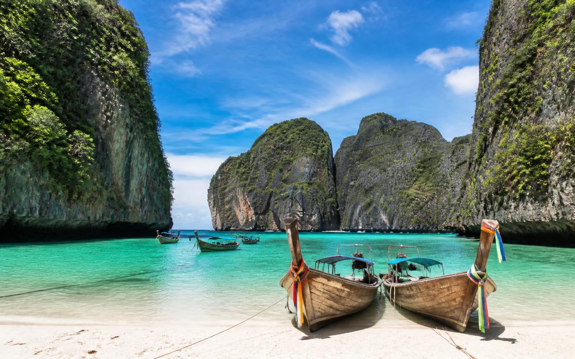 Longtail boats on white sand below limestone karst cliffs and emerald water, Phi Phi Islands, Thailand