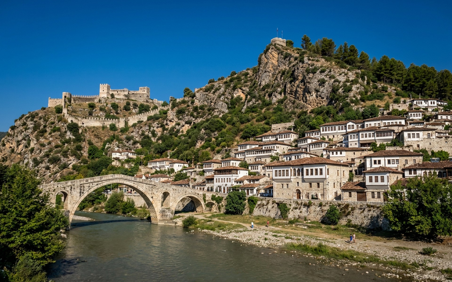 Panoramic view of Berat's historic white Ottoman houses climbing a steep hill towards a medieval castle under a clear summer sky. at Berat & Gjirokastër, Albania — original Triple VIP destination visual.