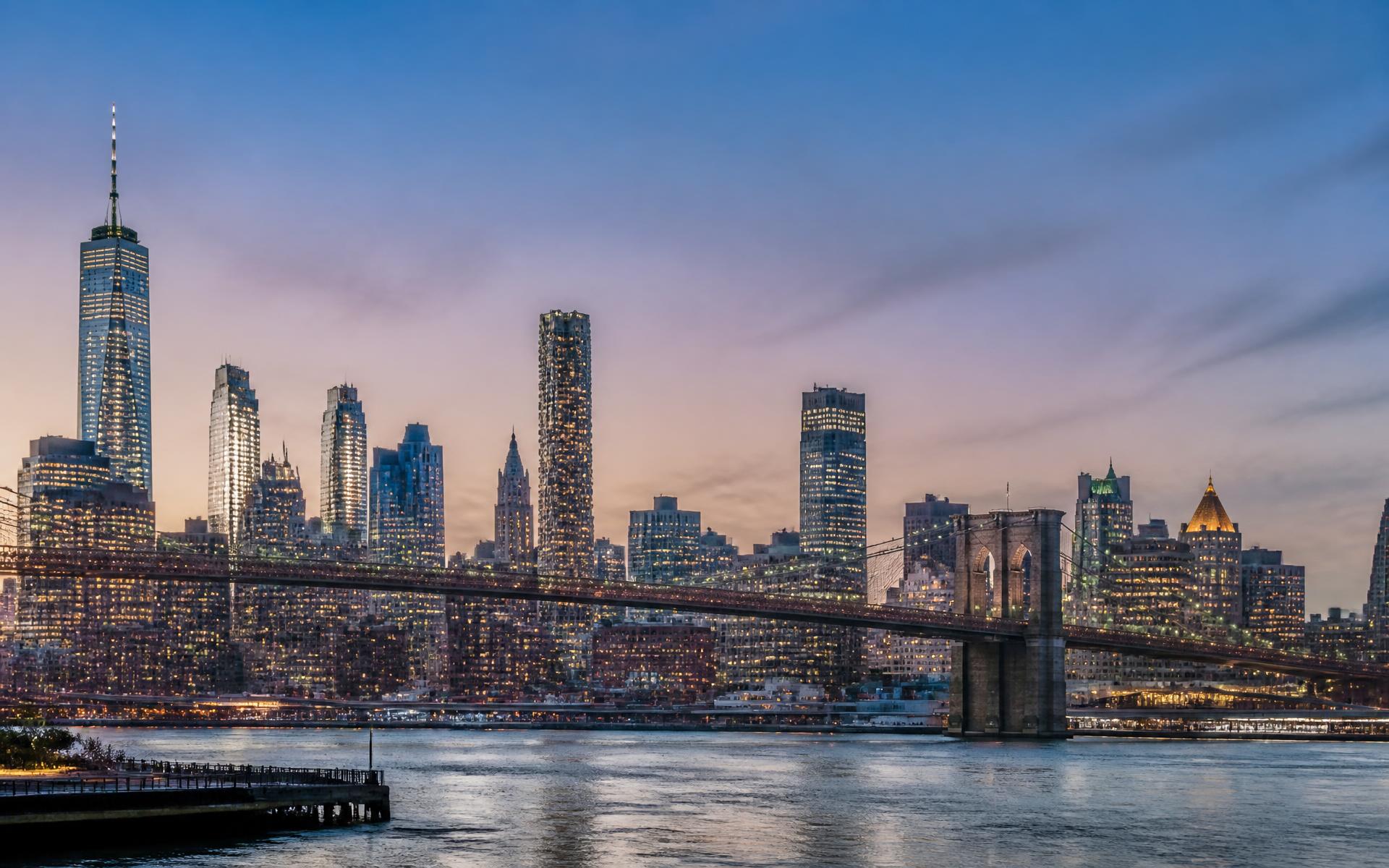 Lower Manhattan skyline and a steel suspension bridge across the East River at blue hour