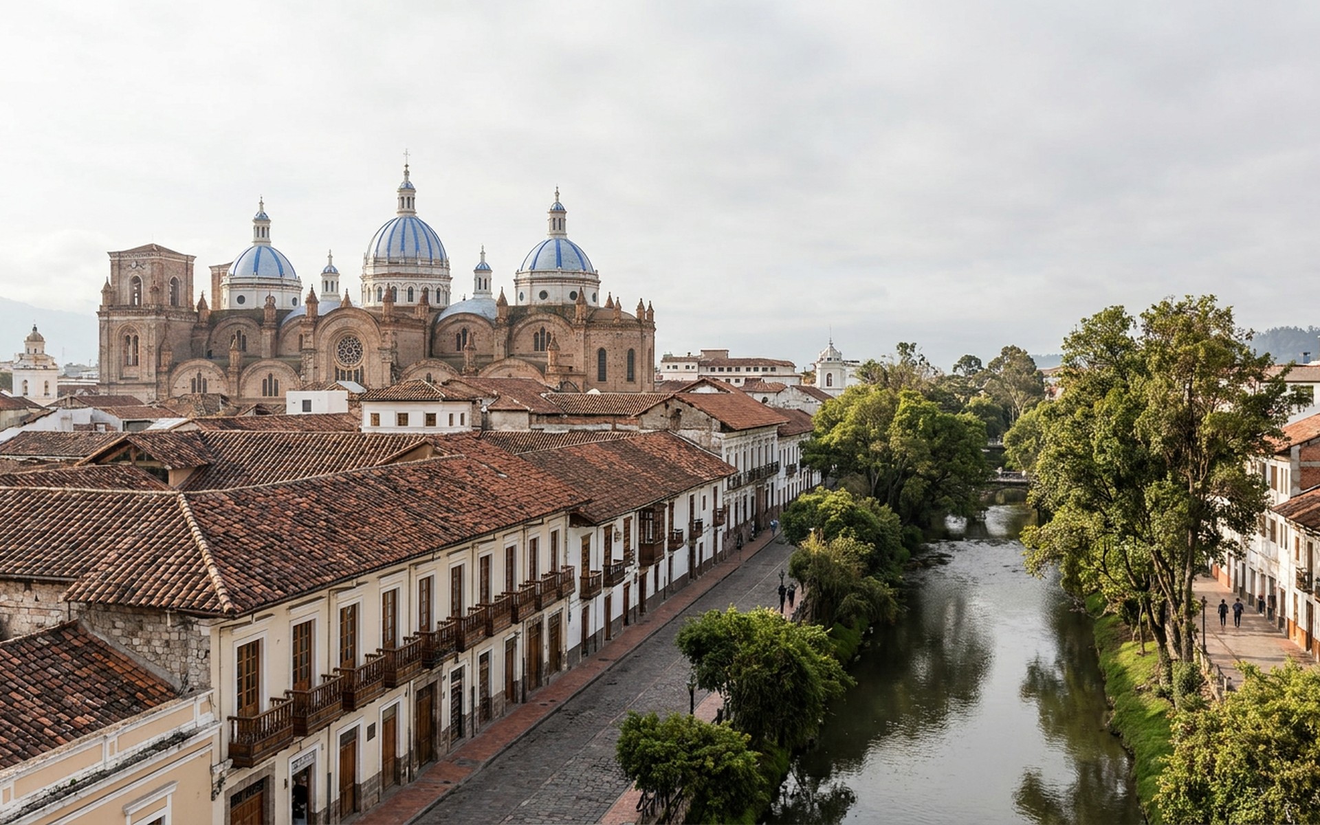 blue-domed cathedral towers above red-tiled colonial roofs and a river-edge street of balconies at Cuenca, Ecuador — original Triple VIP destination visual.