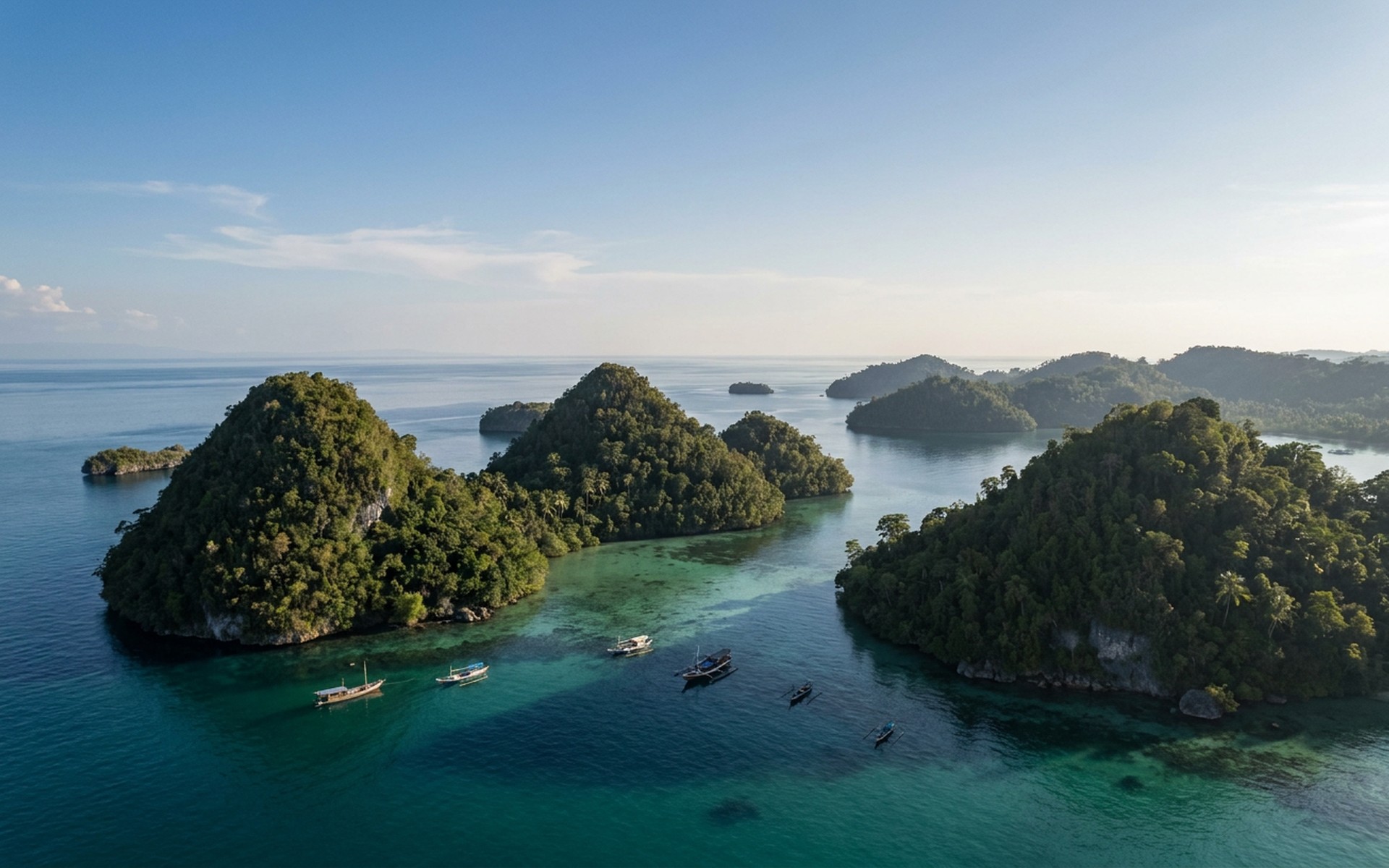 Aerial view of lush green forested islands rising from calm, emerald-blue ocean waters, with small traditional boats anchored offshore, dry season. at Togean Islands, Indonesia — original Triple VIP destination visual.