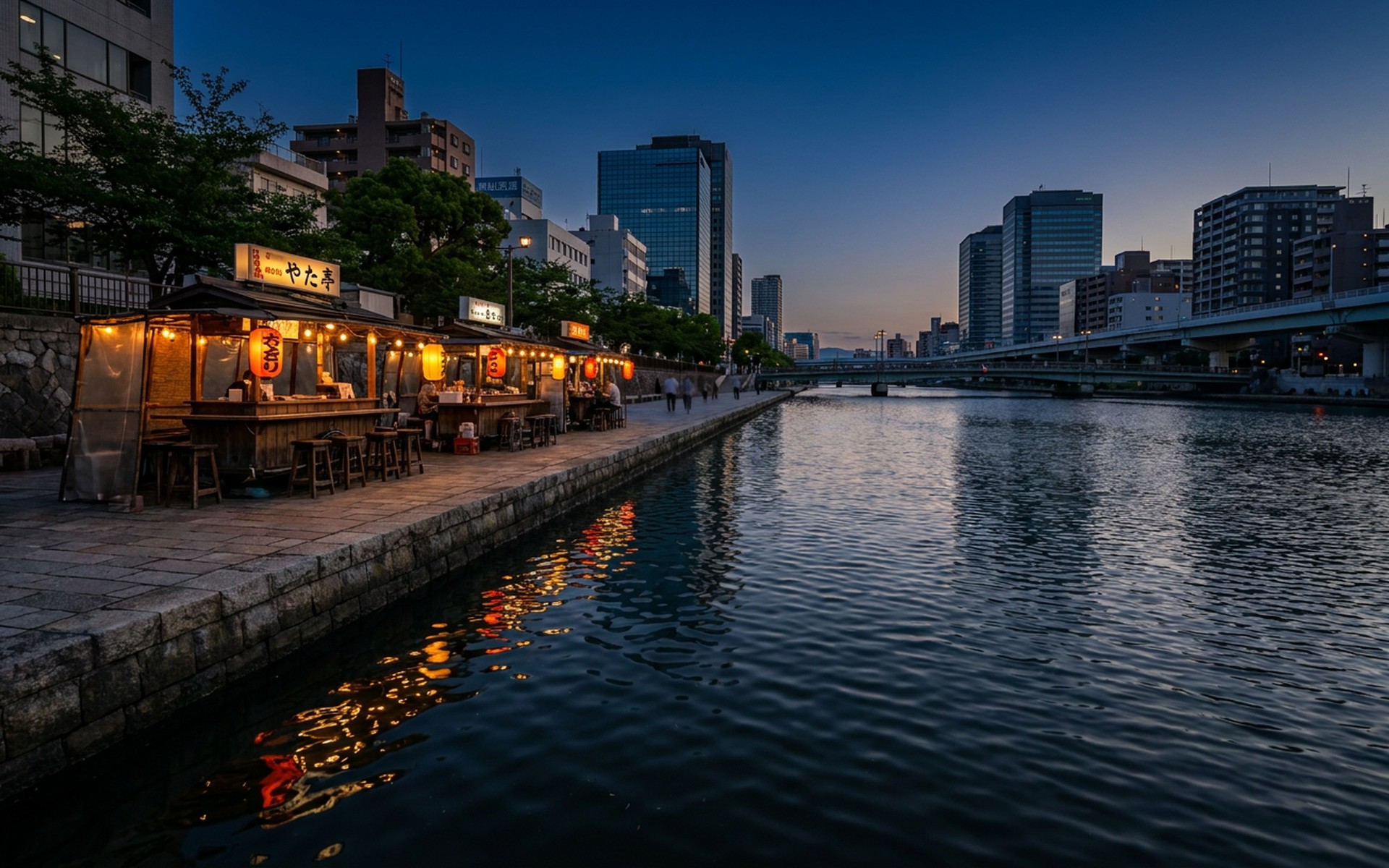 the Naka river waterfront at blue hour with riverside yatai food stalls glowing beneath modern towers at Fukuoka, Japan — original Triple VIP destination visual.