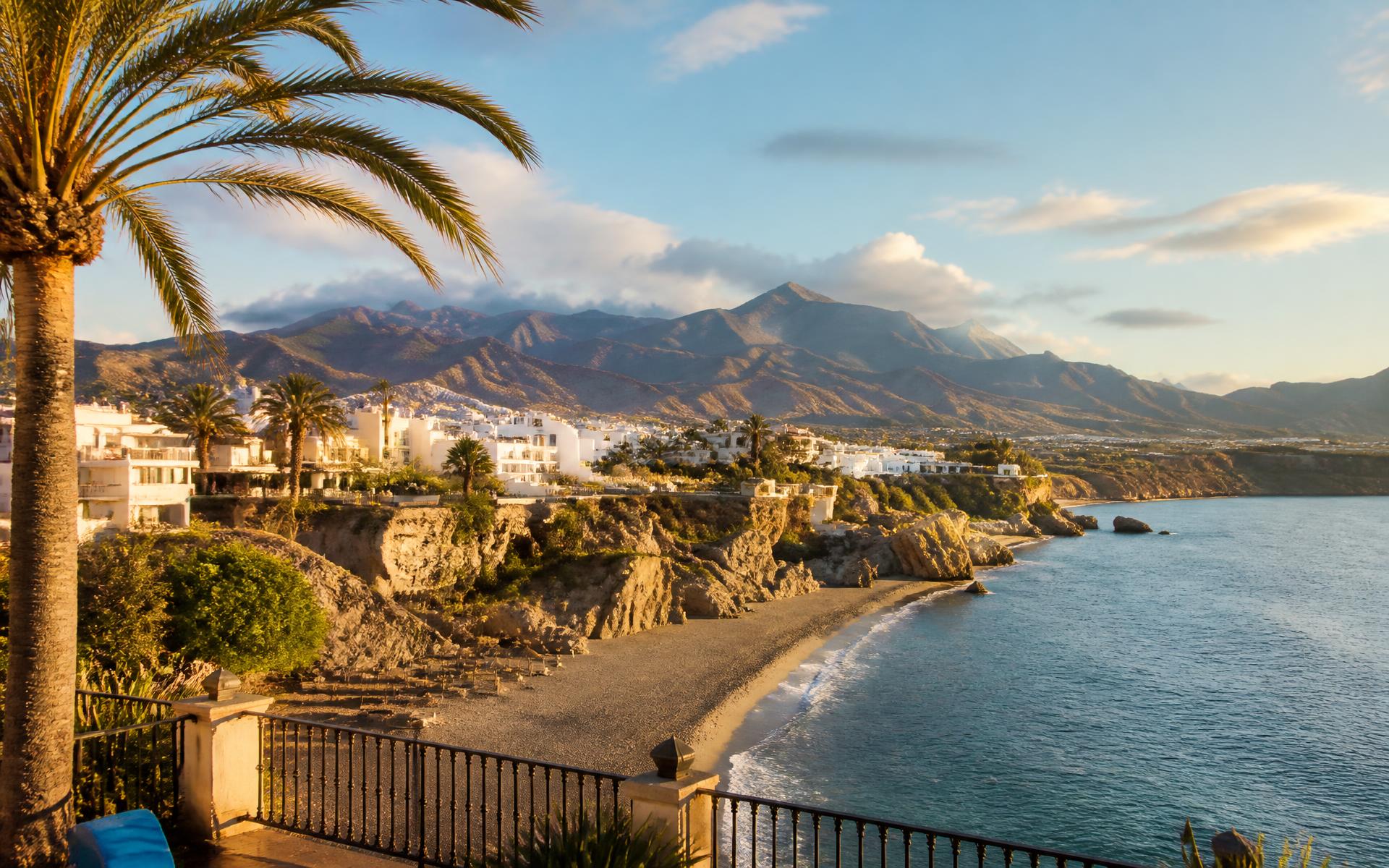 a whitewashed Andalusian coastal town above a broad Mediterranean beach at the Costa del Sol, Spain — original Triple VIP destination visual.
