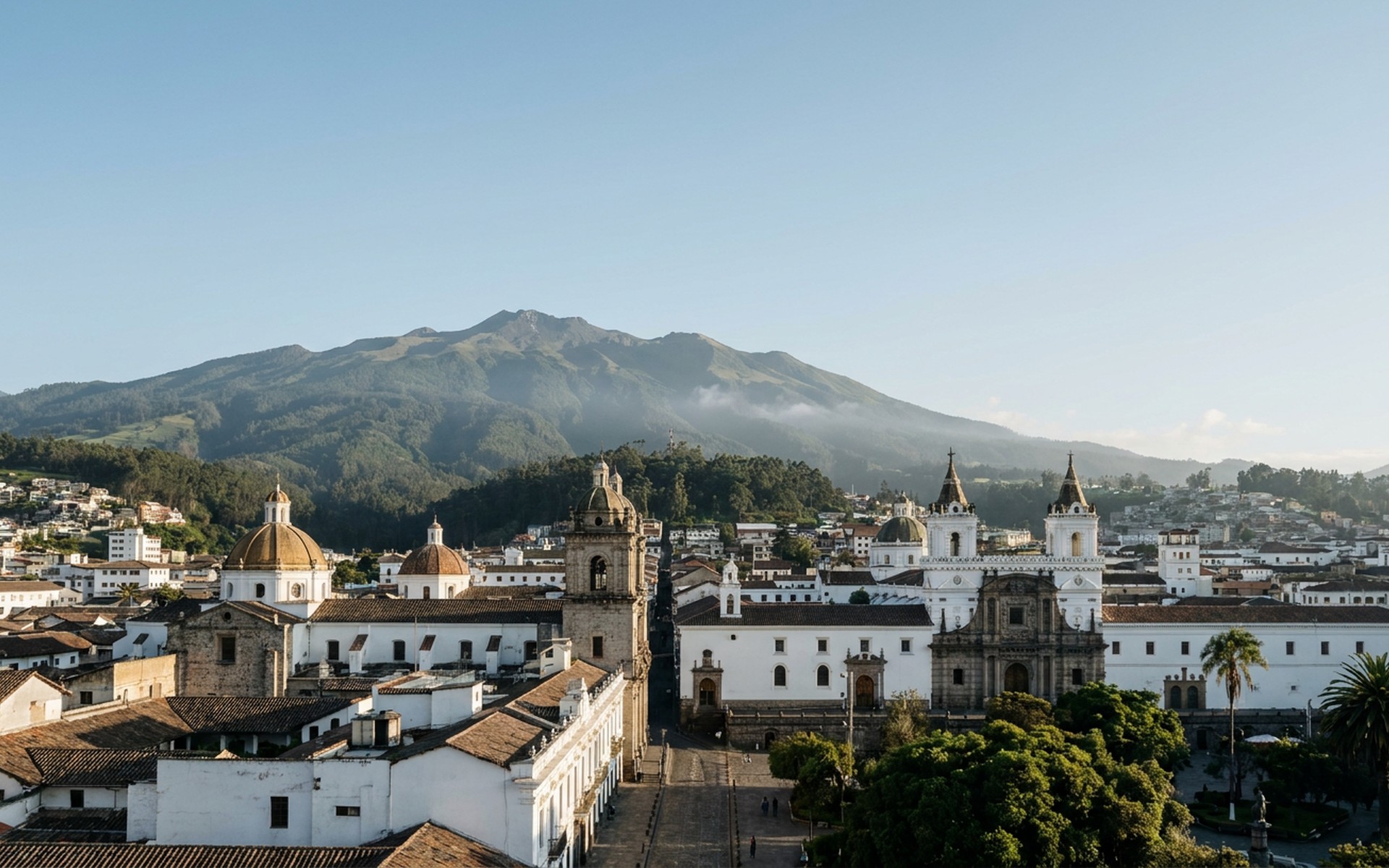 the colonial old town's white-and-ochre domes and bell towers below the green flank of Pichincha volcano at Quito, Ecuador — original Triple VIP destination visual.