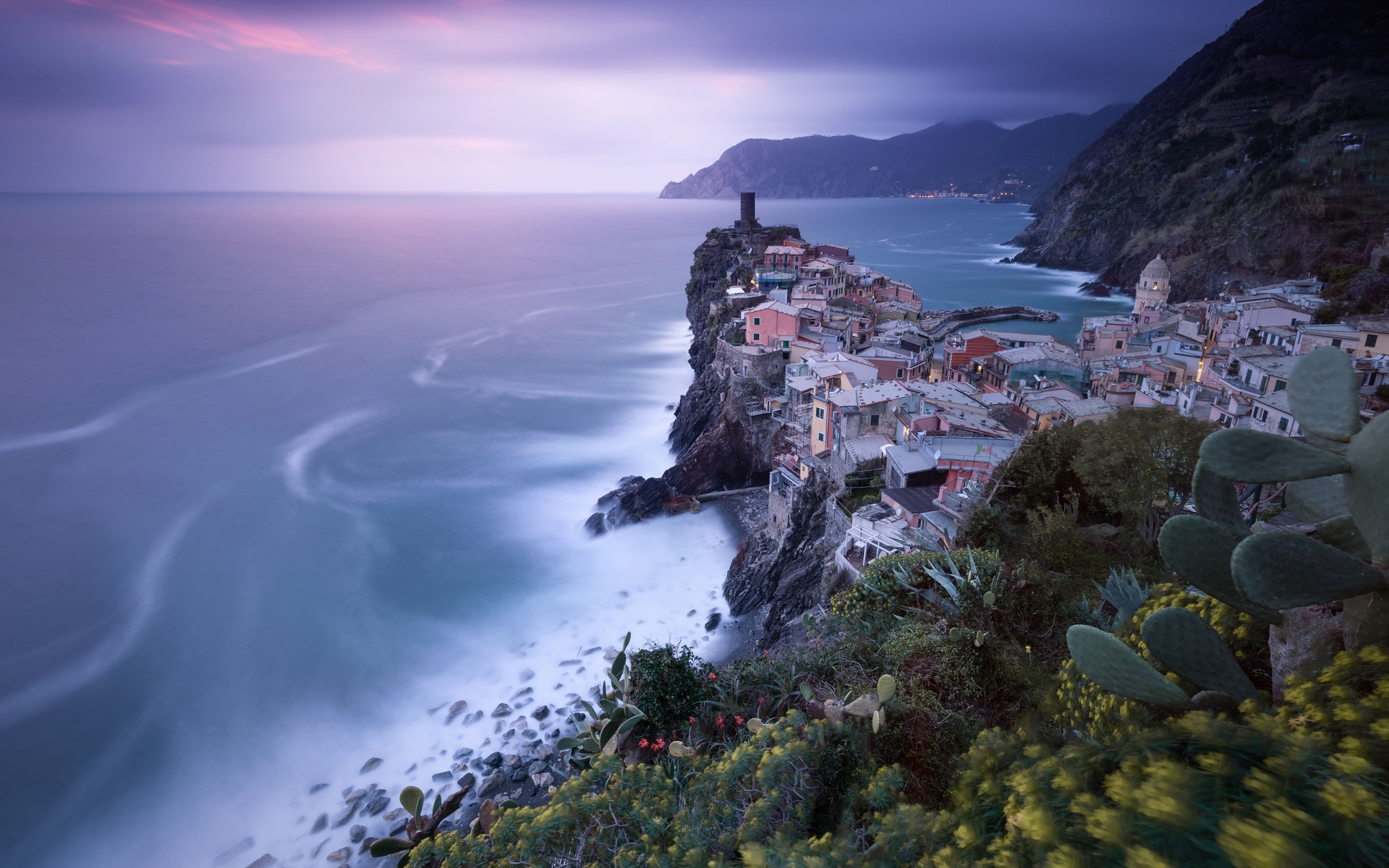 Breathtaking coastal cliff view of Vernazza at twilight, featuring colorful houses and the Mediterranean Sea.
