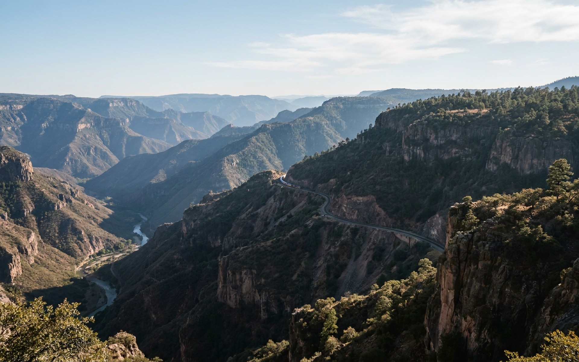 immense layered canyon ridges receding in blue haze with pine-covered rims and a narrow railway ledge at Copper Canyon, Mexico — original Triple VIP destination visual.