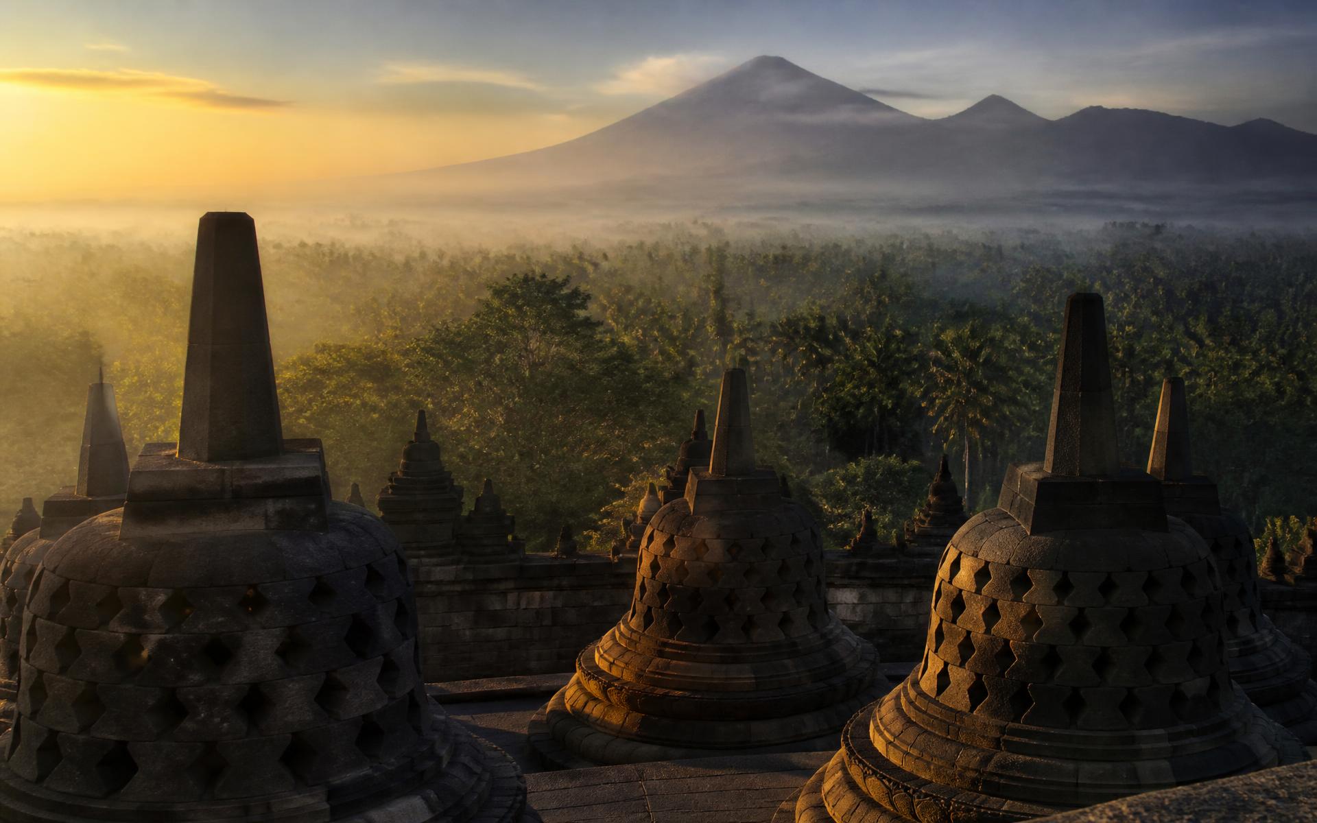 the stepped stone stupas of Borobudur above jungle and volcanoes at sunrise at Yogyakarta, Indonesia — original Triple VIP destination visual.
