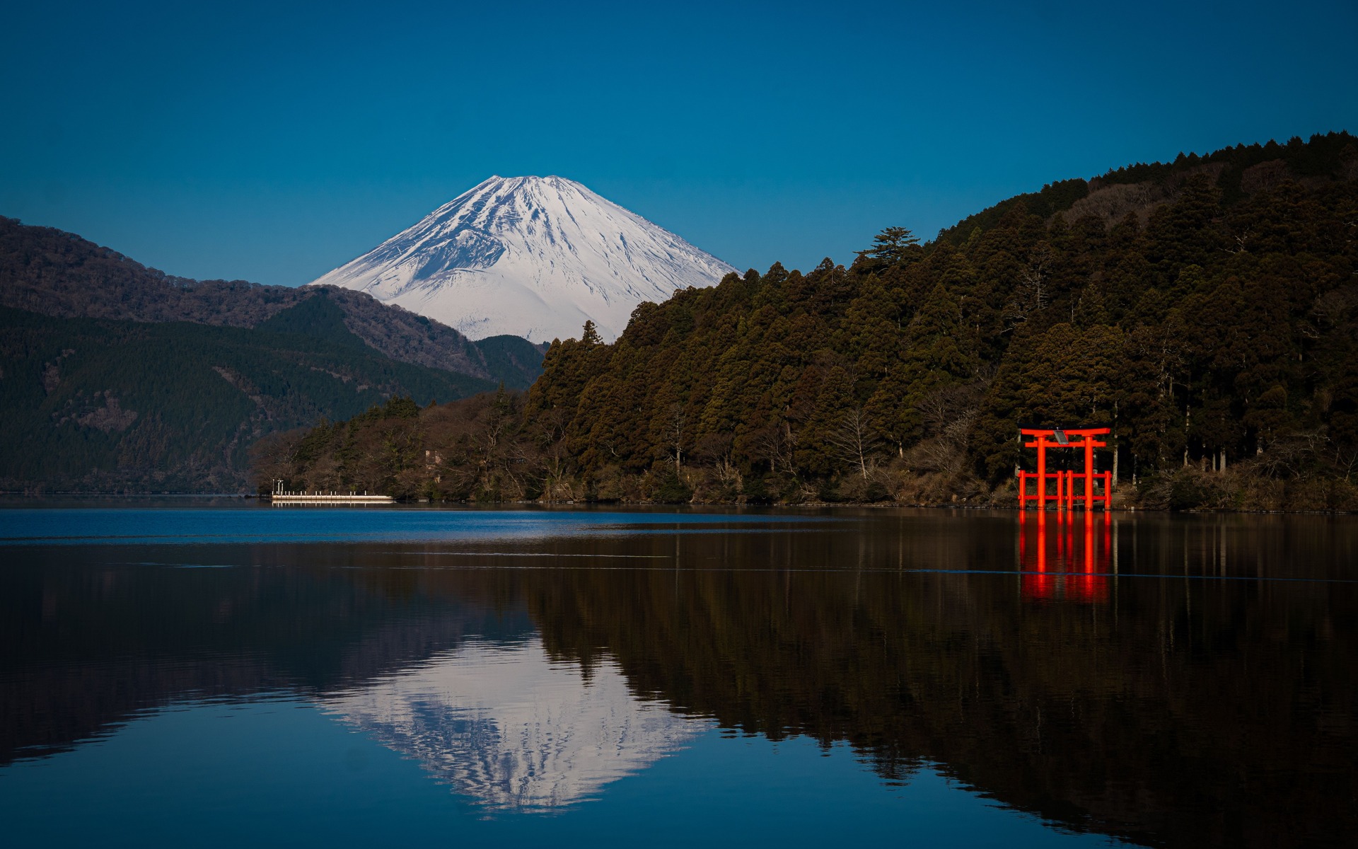Stunning view of Mount Fuji and a red torii gate reflecting in Lake Ashi, Hakone, Japan.