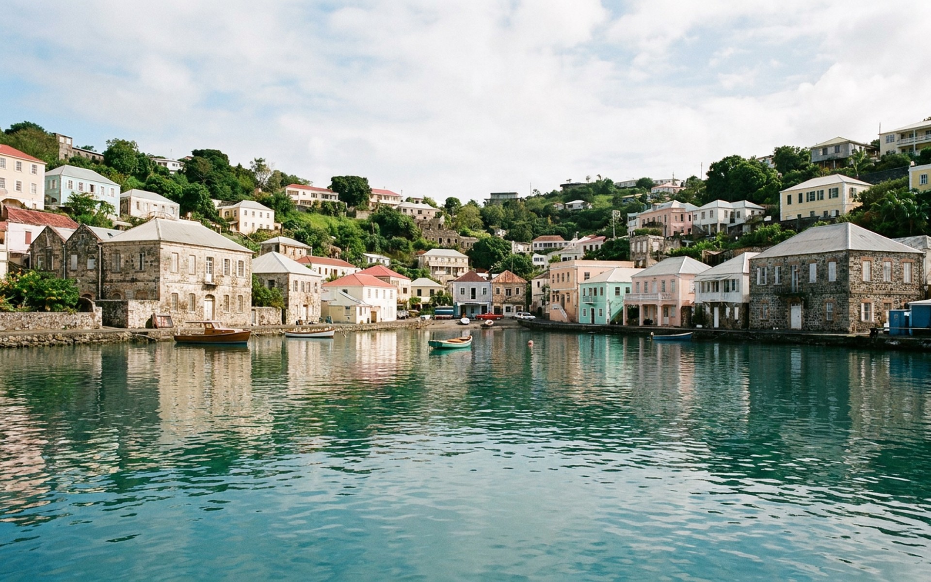 a calm horseshoe bay with pastel harbour houses on a green hillside and clear turquoise water at Grenada — original Triple VIP destination visual.
