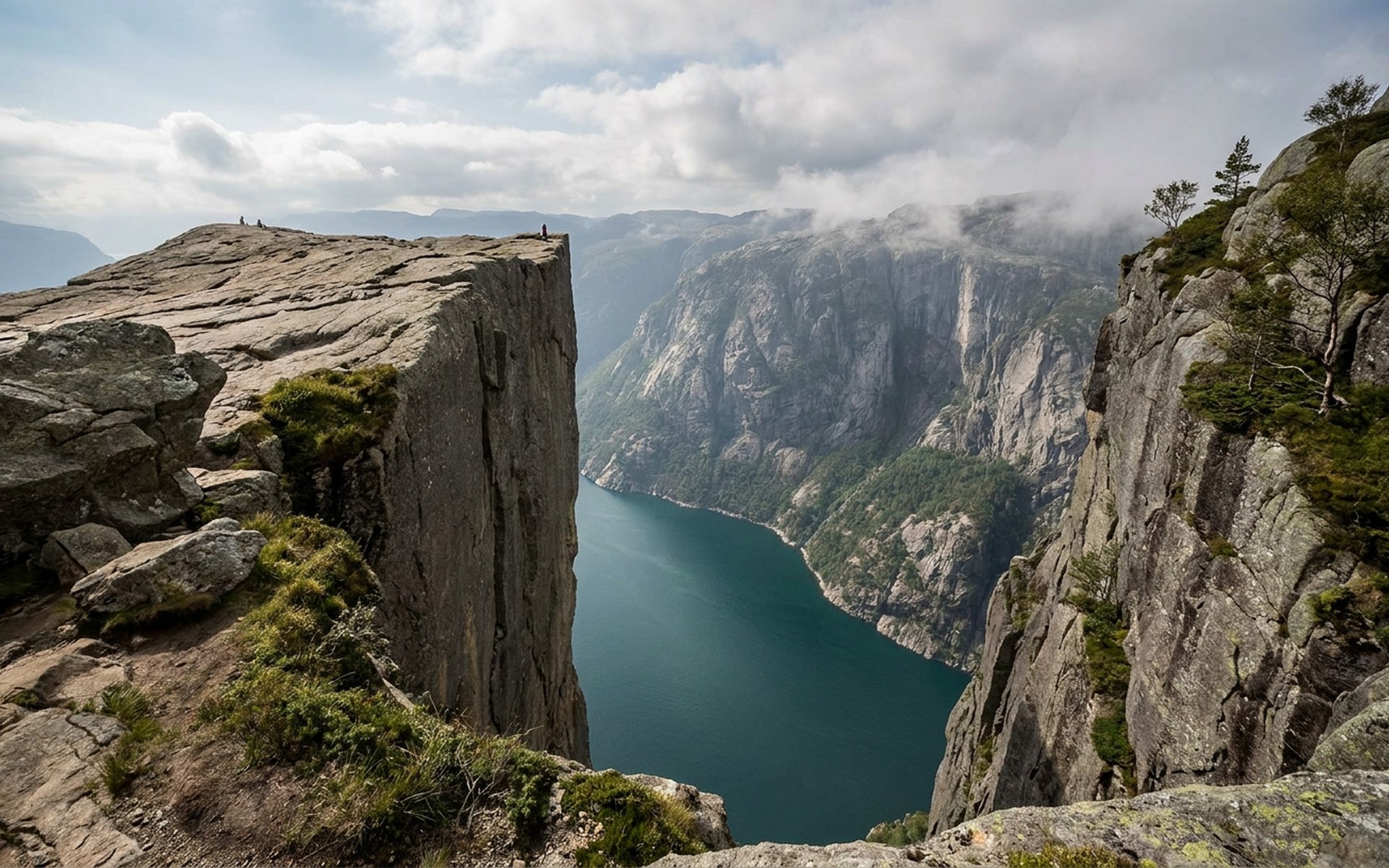 a flat rock ledge jutting over a deep narrow fjord a thousand metres below with sheer grey walls opposite at Lysefjord, Norway — original Triple VIP destination visual.