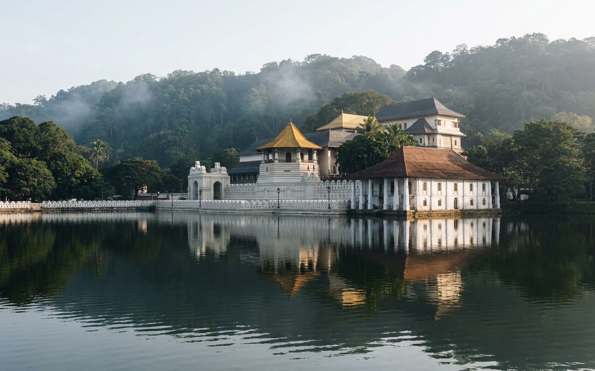 a white colonnaded temple pavilion with a golden roof beside a still lake ringed by misty forested hills at Kandy, Sri Lanka — original Triple VIP destination visual.
