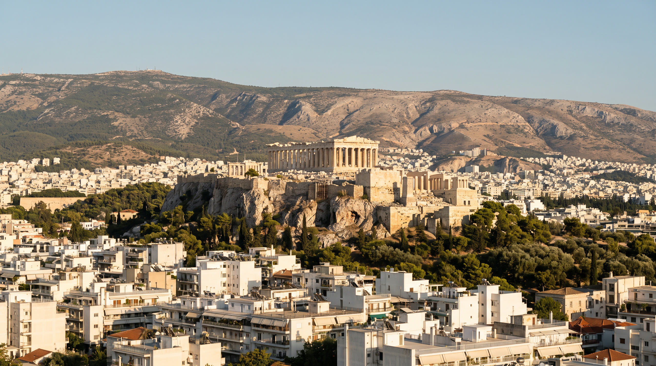 the Acropolis limestone outcrop above the low white city at Athens, Greece, in late afternoon light — original Triple VIP destination visual.
