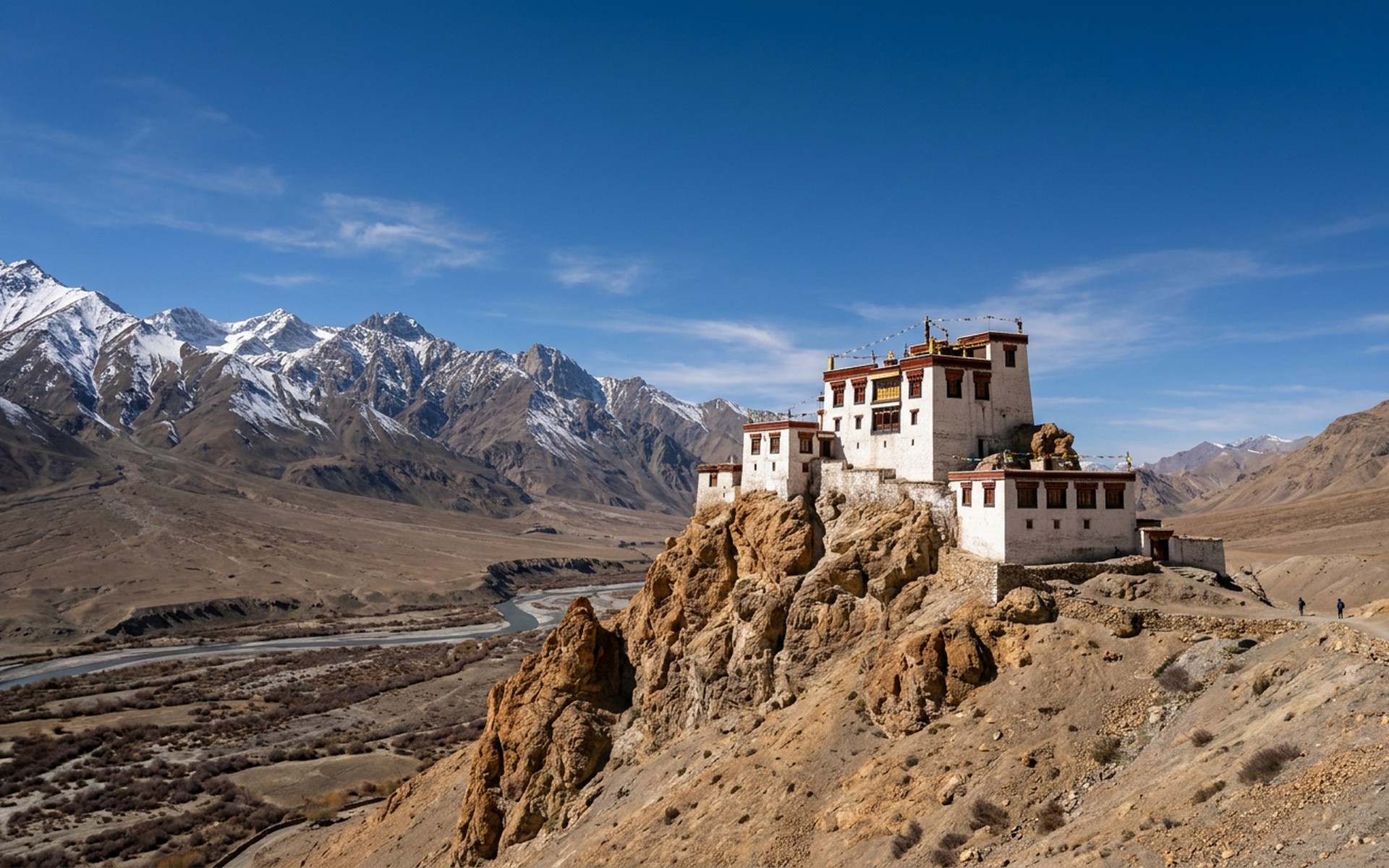 a whitewashed Tibetan-Buddhist monastery on a rock spur above a barren ochre valley and snow peaks at Ladakh, India — original Triple VIP destination visual.