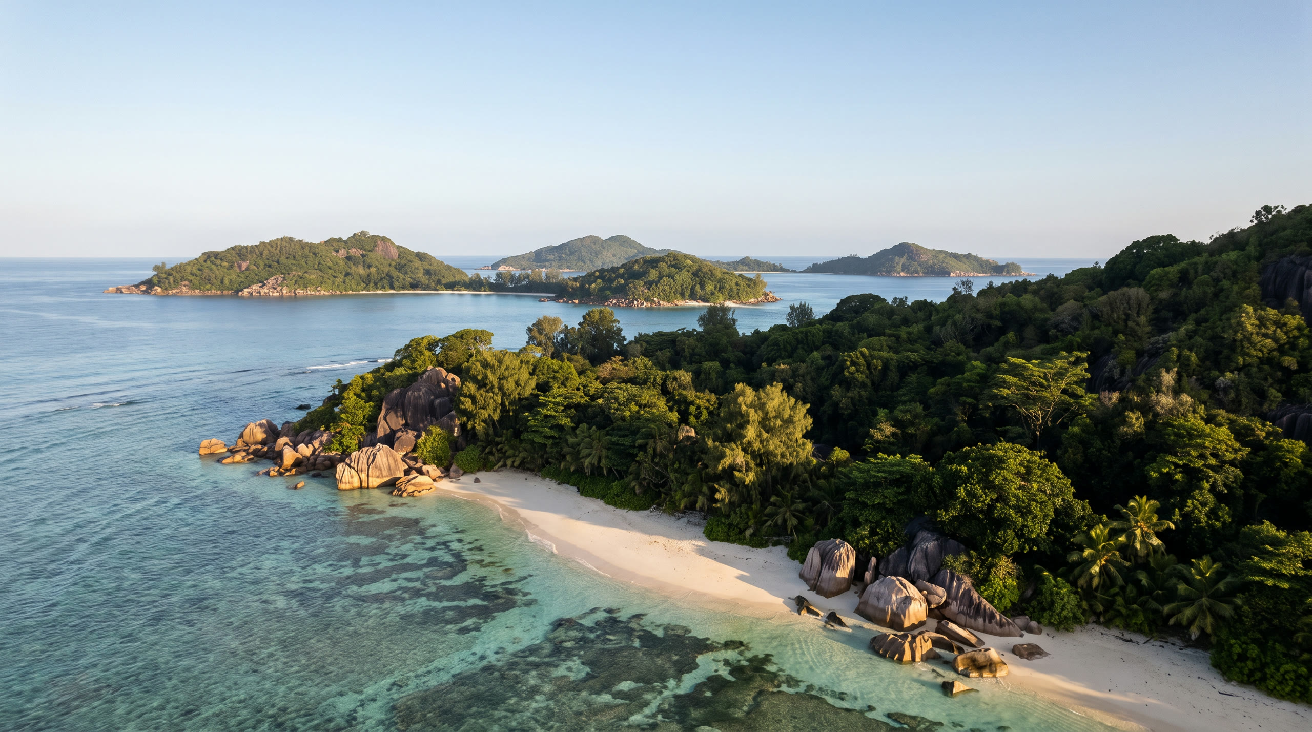 granite boulders on a pale beach with clear shallow water and takamaka trees at Seychelles, Seychelles, in morning light — original Triple VIP destination visual.