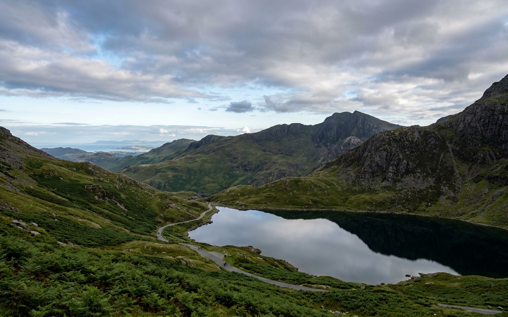 Majestic peaks of Snowdonia National Park, with lush green valleys and a serene lake reflecting the rugged landscape under a dramatic sky. at Snowdonia & the North Wales Coast, United Kingdom — original Triple VIP destination visual.