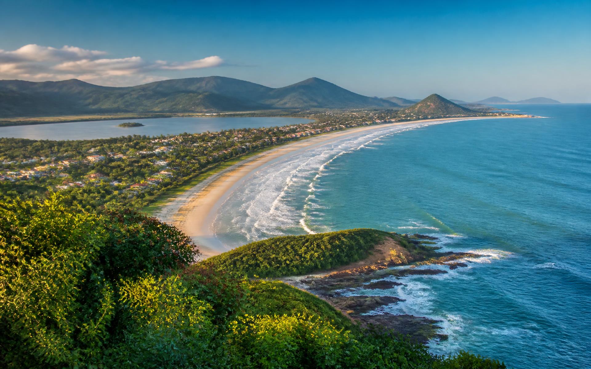 a crescent surf beach between forested headlands with an island city beyond at Florianópolis, Brazil — original Triple VIP destination visual.