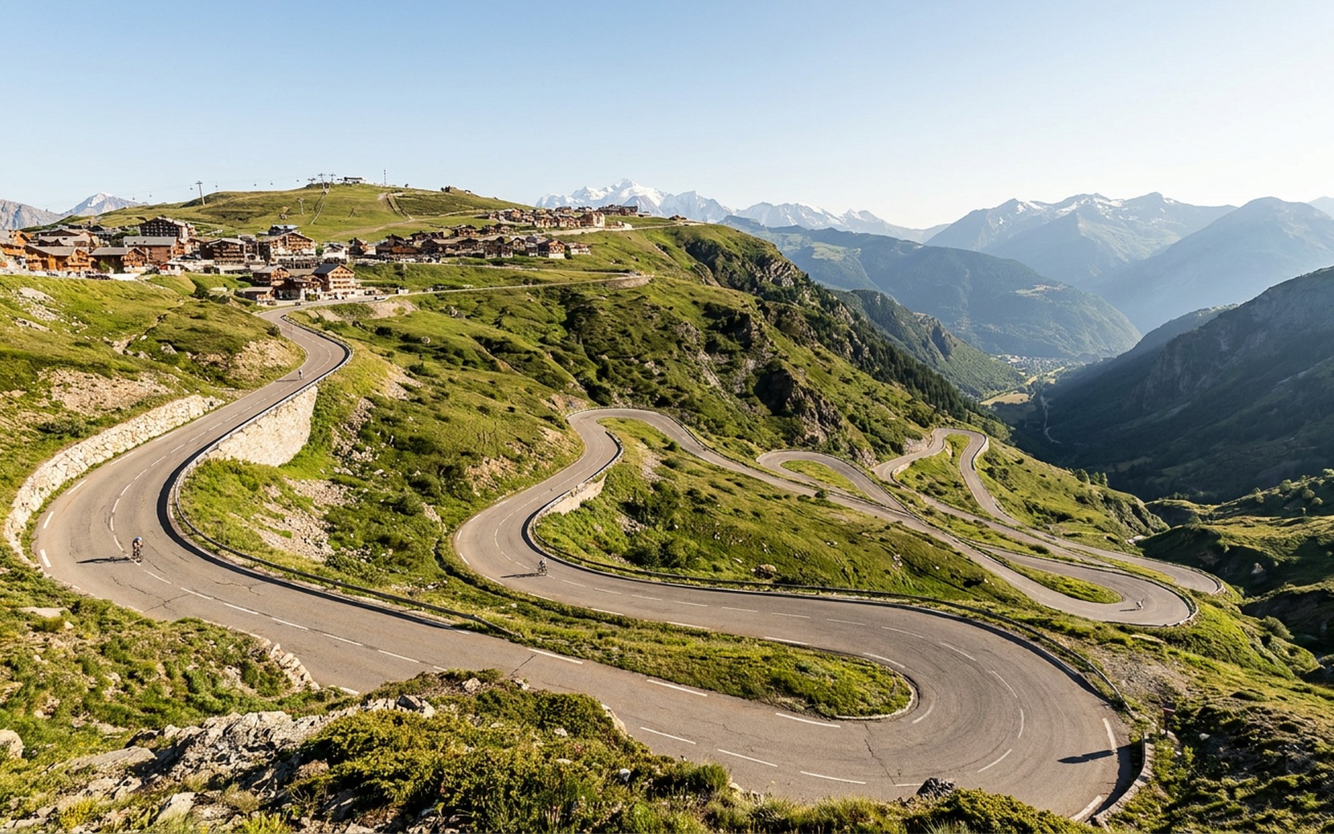 The iconic hairpin bends of the cycling climb, carved into the mountainside, contrasting with snow-capped peaks under a clear summer sky. at Alpe d'Huez, France — original Triple VIP destination visual.