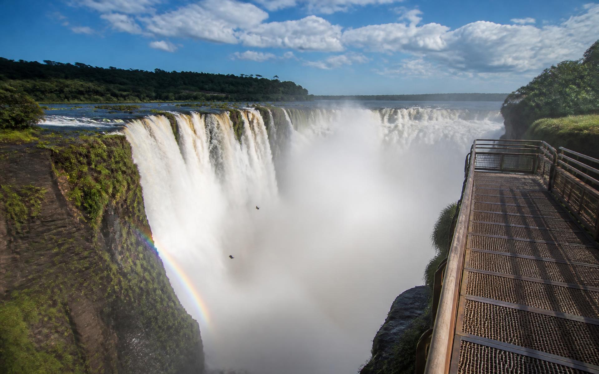 the Devil's Throat horseshoe seen from close above on the Argentine catwalk, a single vast curtain of water falling into a column of spray at Iguazú — Argentine Side, Argentina, in early afternoon light — original Triple VIP destination visual.