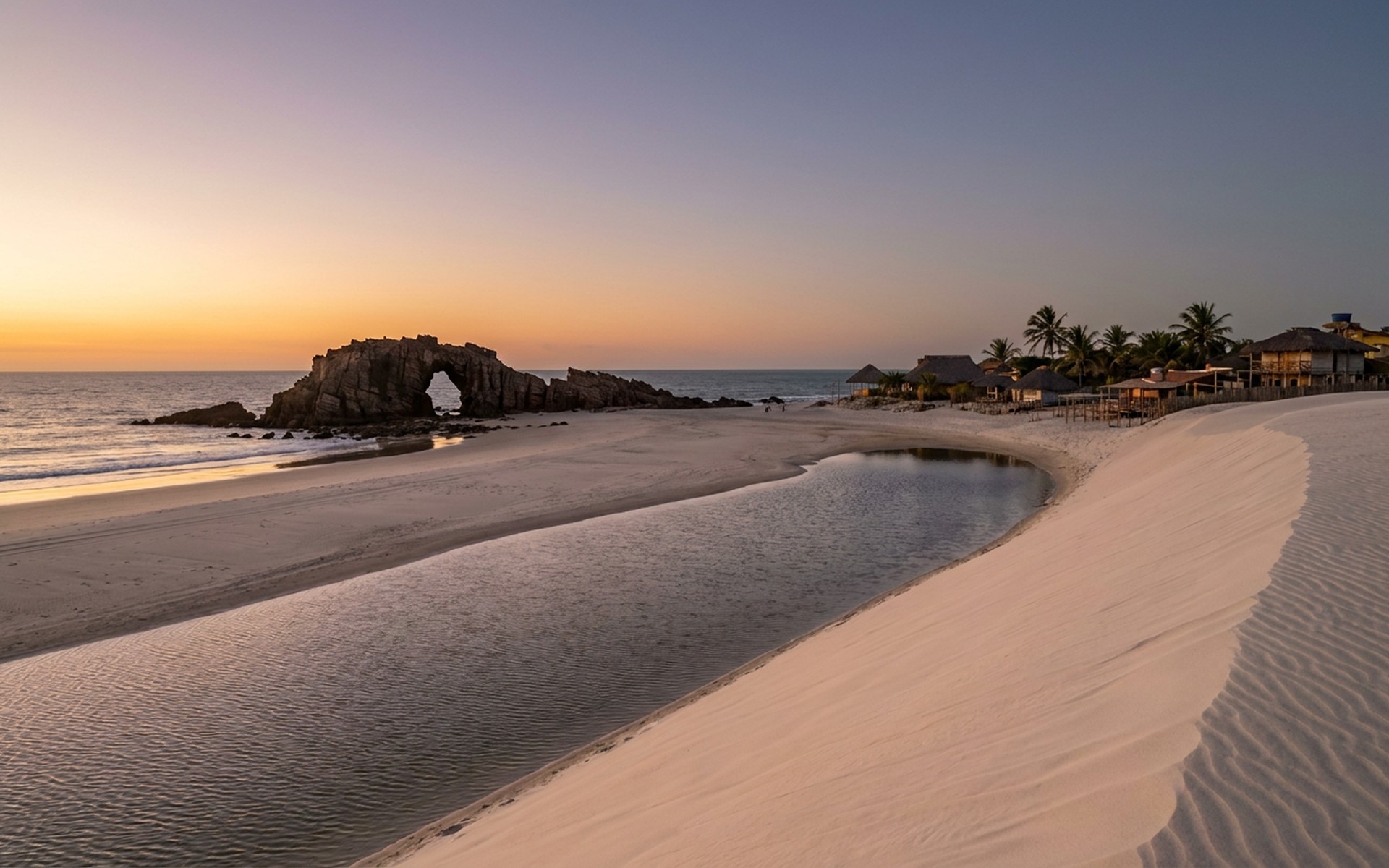 tall white sand dunes meeting a wide beach and freshwater lagoon with a natural stone sea arch at sunset at Jericoacoara, Brazil — original Triple VIP destination visual.
