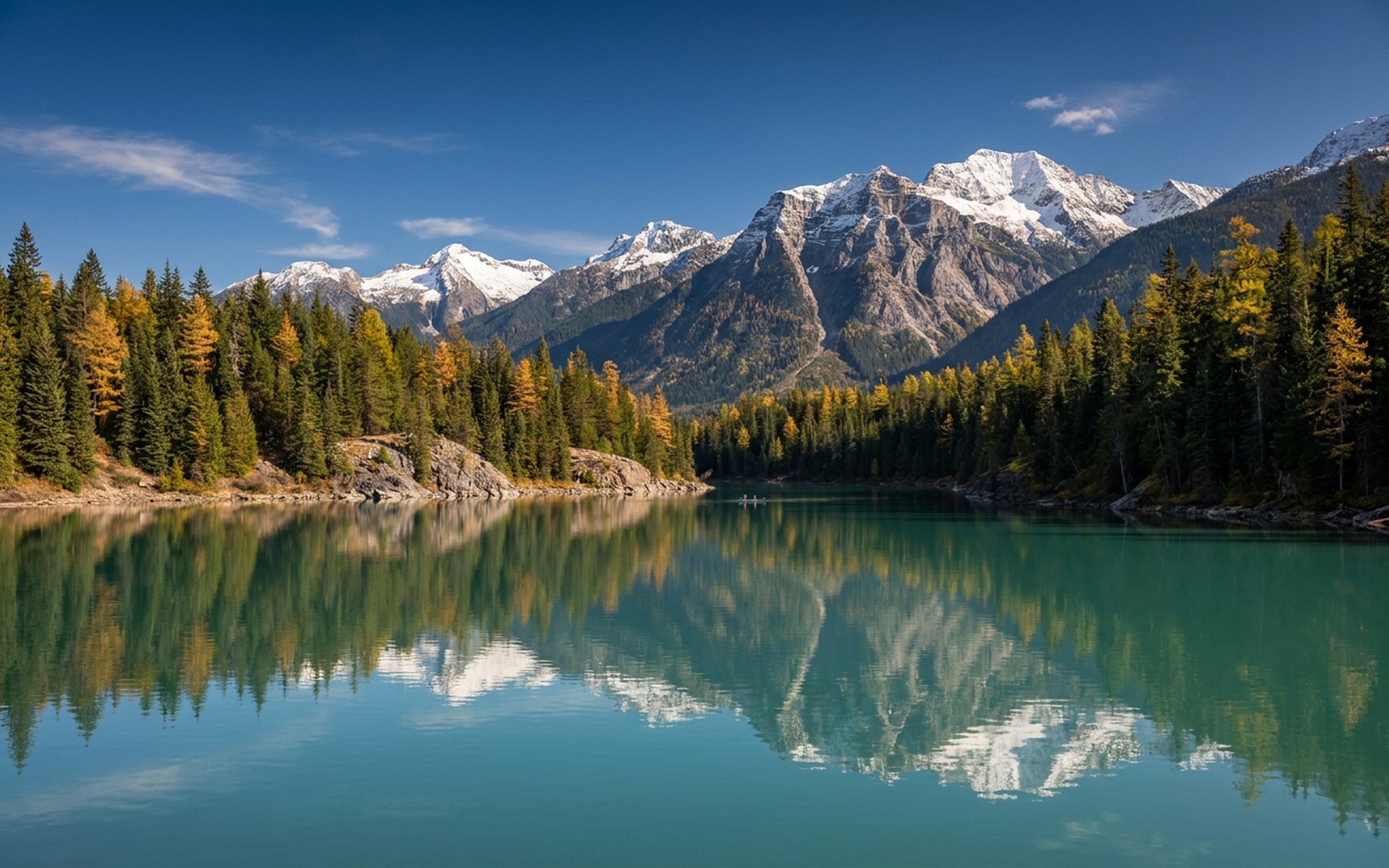 Lush evergreen forests and the snow-capped peaks of the Monashee Mountains reflected in a pristine glacial lake under a clear, crisp autumn sky. at Revelstoke, Canada — original Triple VIP destination visual.