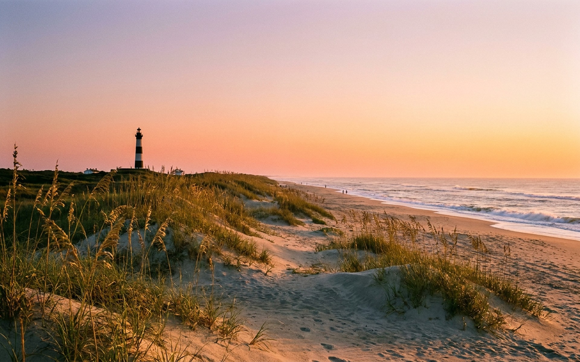 Sunrise illuminating the sandy dunes and sea oats along the Atlantic coastline, with a distant lighthouse silhouette against the vibrant orange sky in summer. at Outer Banks, United States — original Triple VIP destination visual.