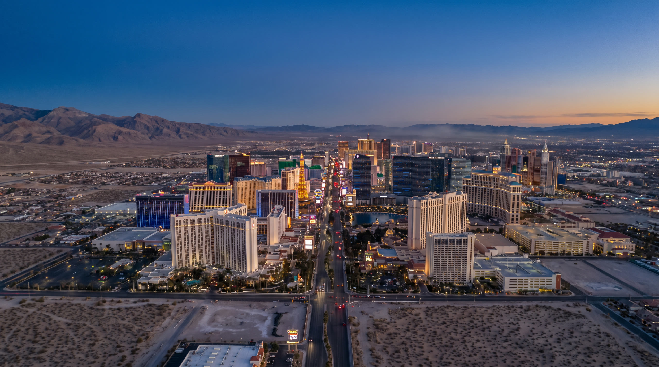 the Strip's illuminated towers against the Mojave desert ranges at Las Vegas, United States, in blue hour light — original Triple VIP destination visual.