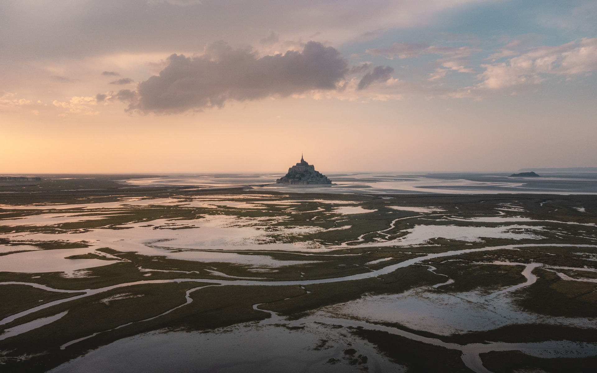 Stunning aerial view of Le Mont-Saint-Michel during low tide at sunset with reflective marshlands.