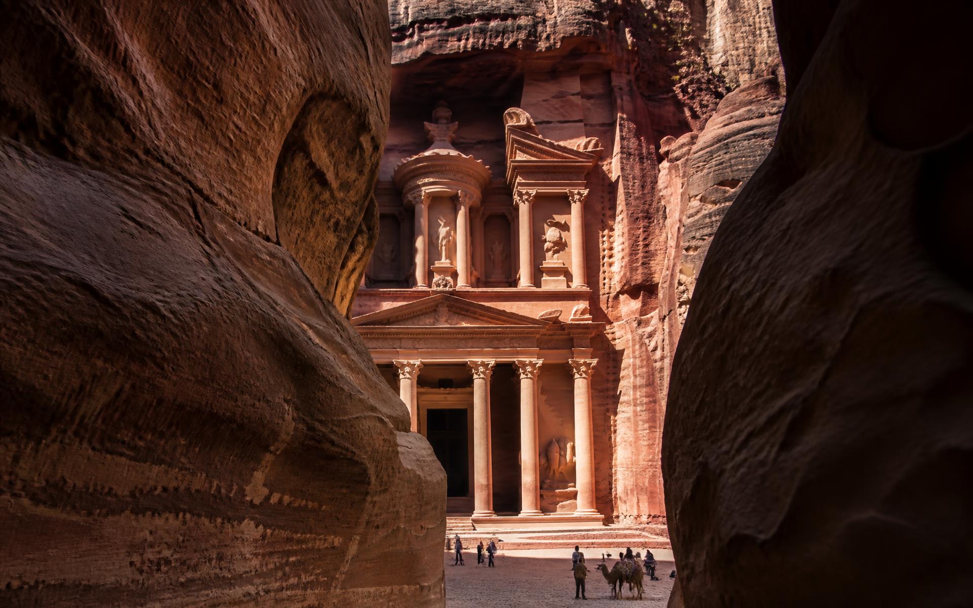 Rock-cut Nabataean treasury façade in rose sandstone framed by the shadowed walls of the siq canyon in Petra