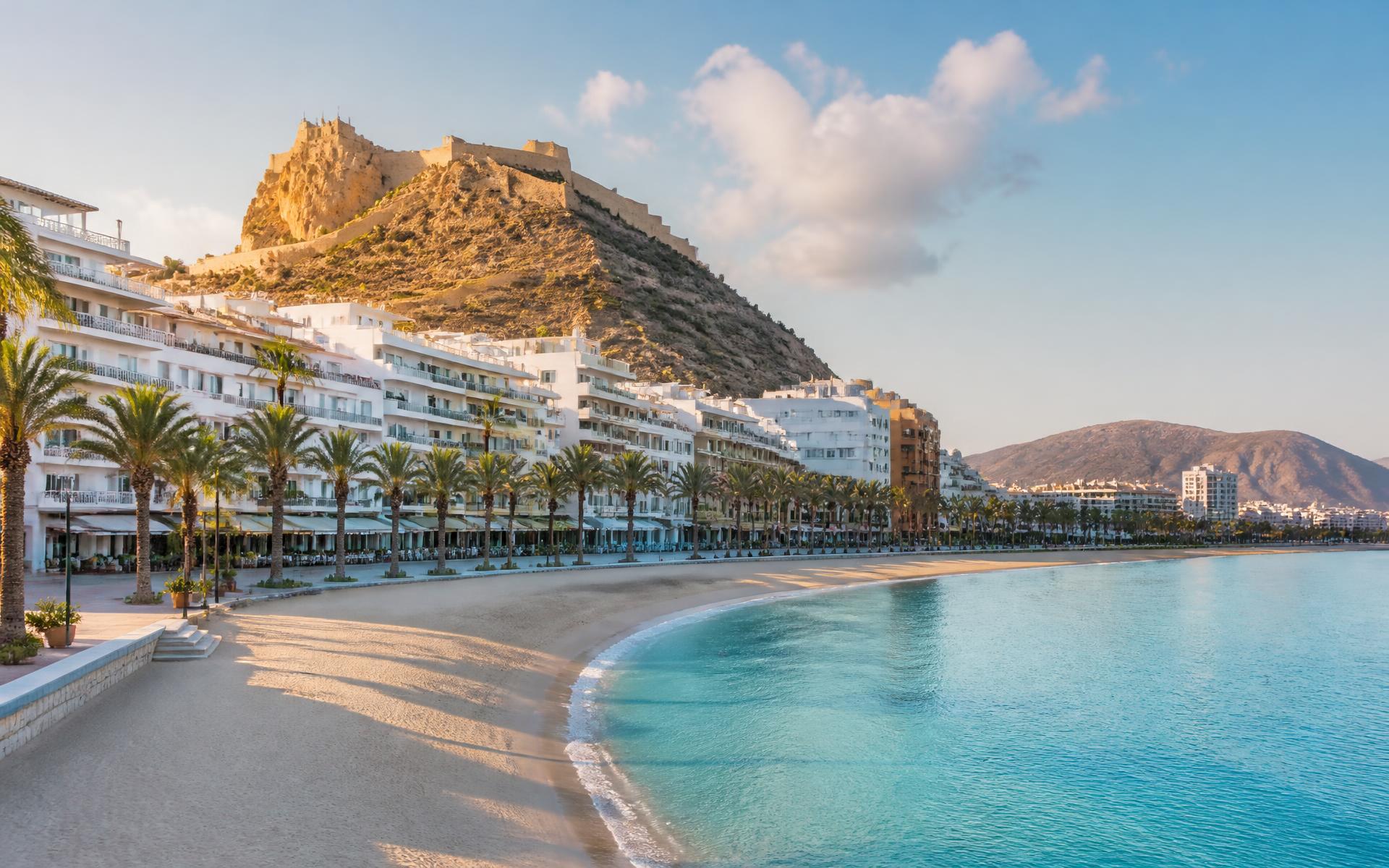 a rocky Mediterranean headland above a turquoise cove and whitewashed town at the Costa Blanca, Spain — original Triple VIP destination visual.