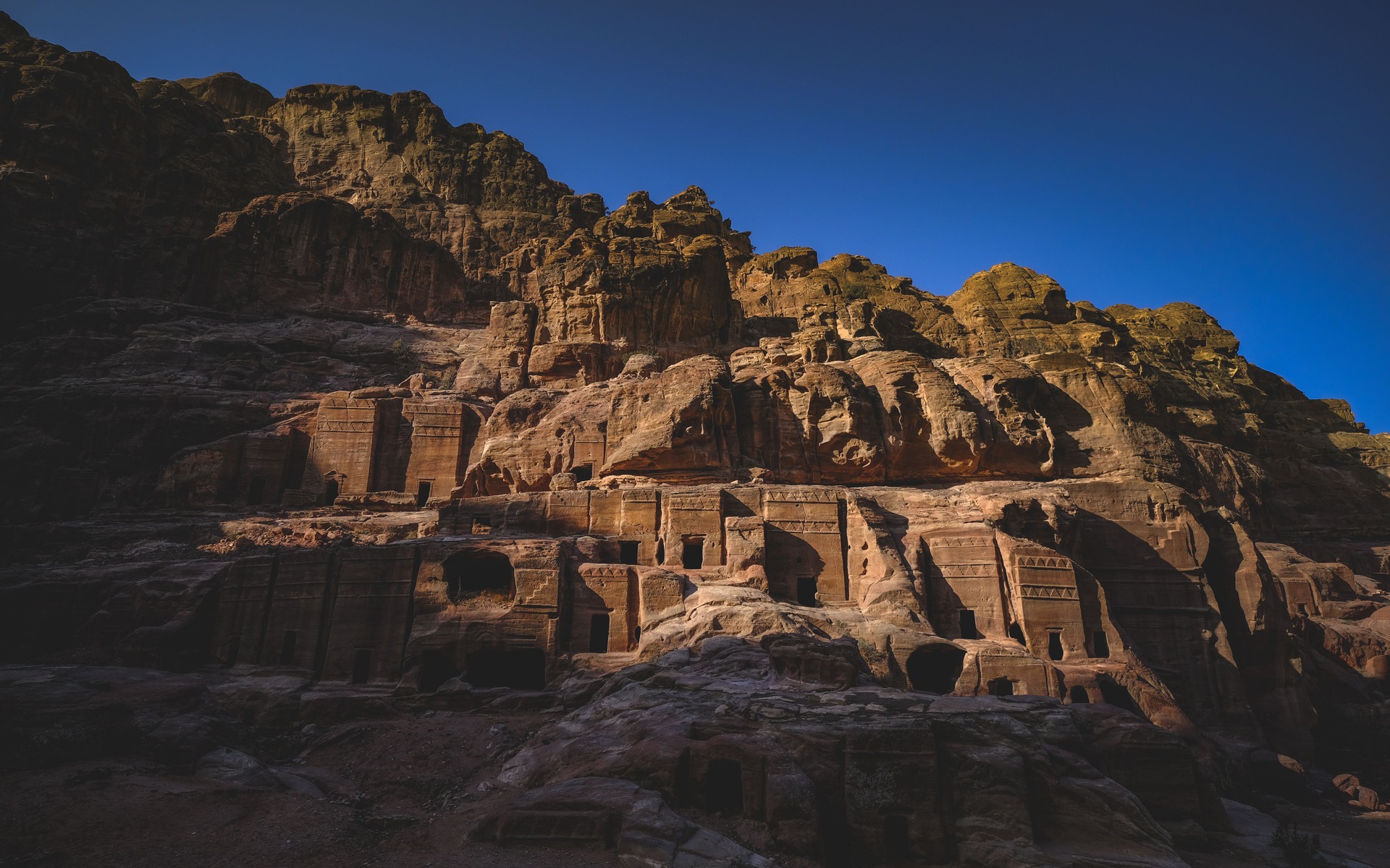 Historic rock-carved buildings sunlit against clear blue sky in Petra, Jordan.