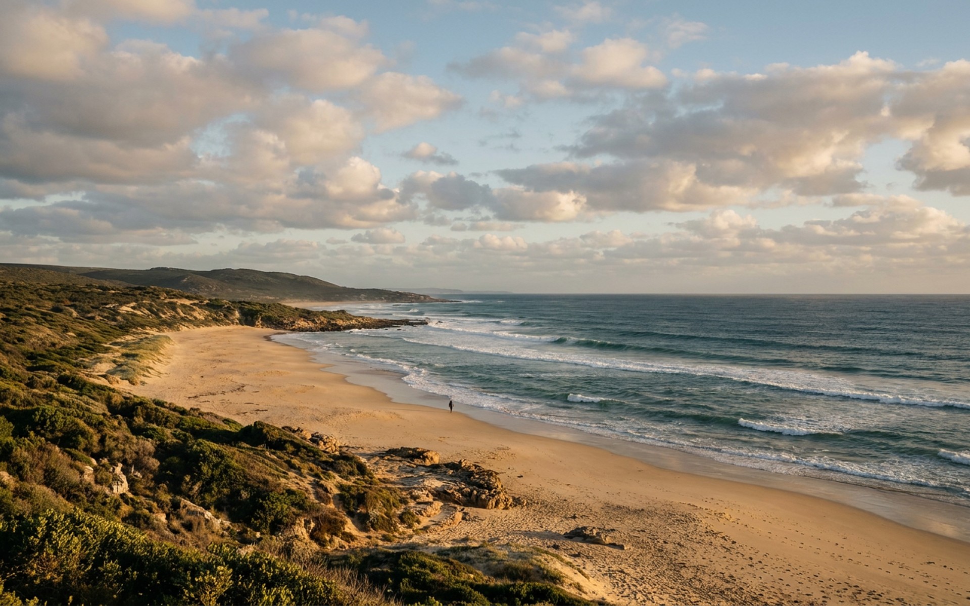 Long, powerful surf breaks peeling rhythmically along a wide sandy beach, with a dramatic coastline visible under a dynamic morning sky. at Jeffreys Bay, South Africa — original Triple VIP destination visual.