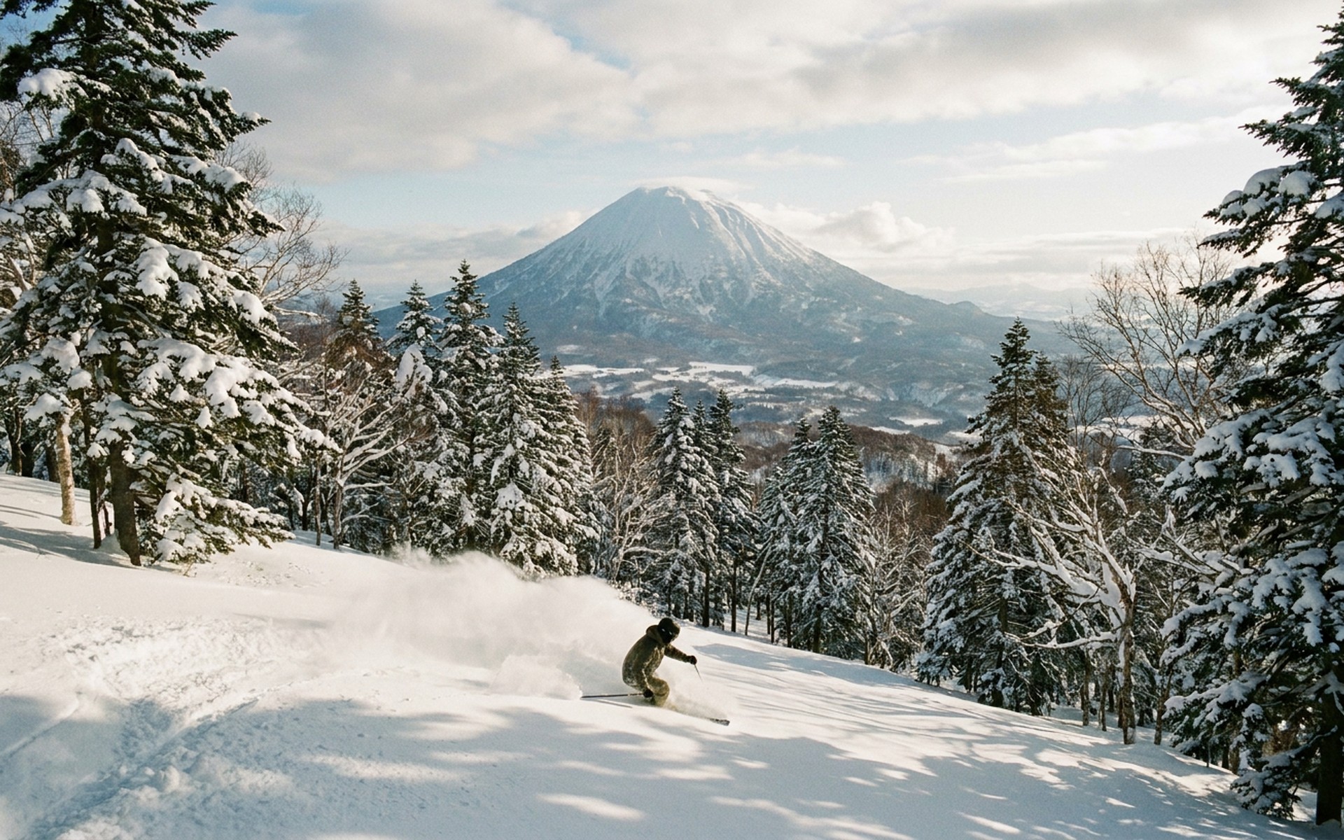 Powder snow exploding around a skier making turns down a pristine, tree-lined slope of Mount Yotei in Hokkaido. at Rusutsu, Japan — original Triple VIP destination visual.
