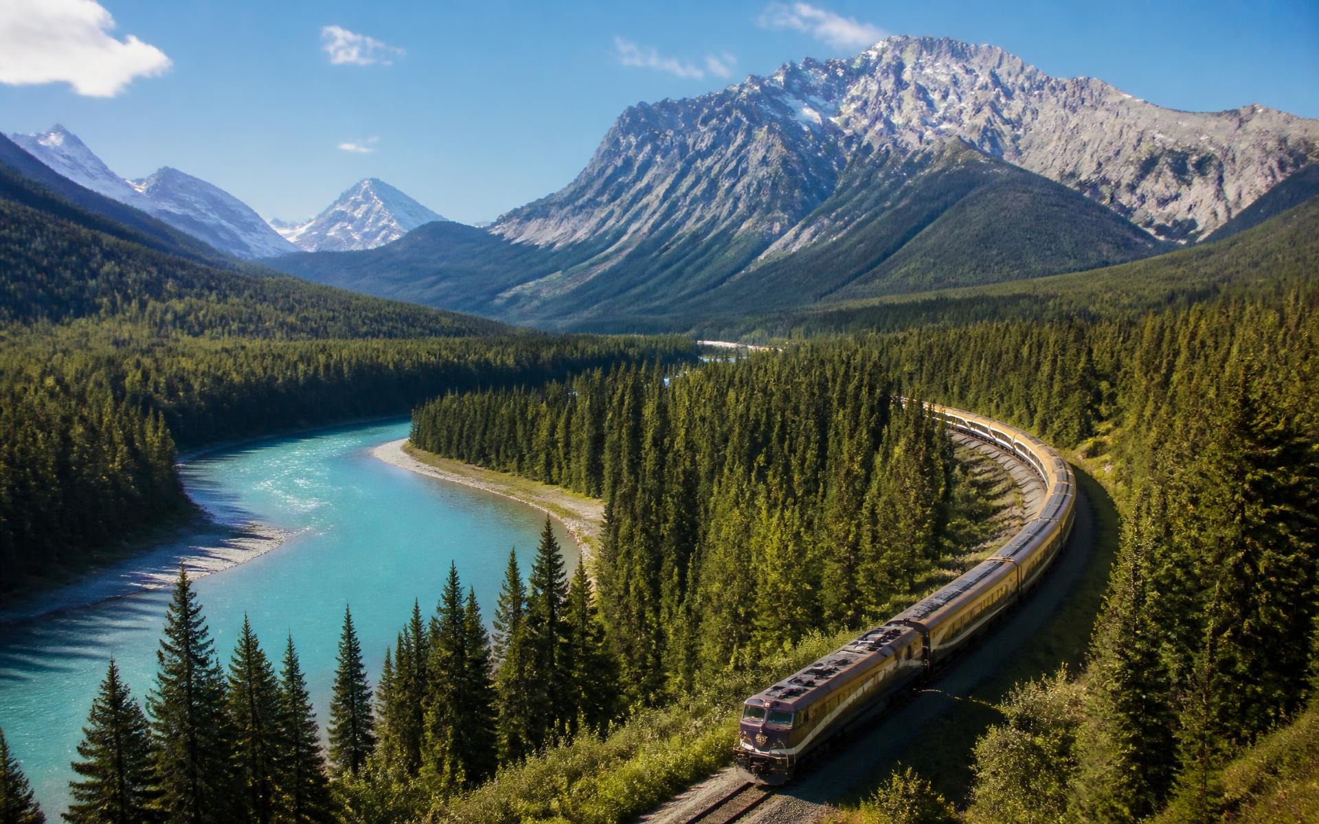 a long train curving through forest beside a turquoise glacial river below snow-capped peaks at the Canadian Rockies rail route — original Triple VIP destination visual.