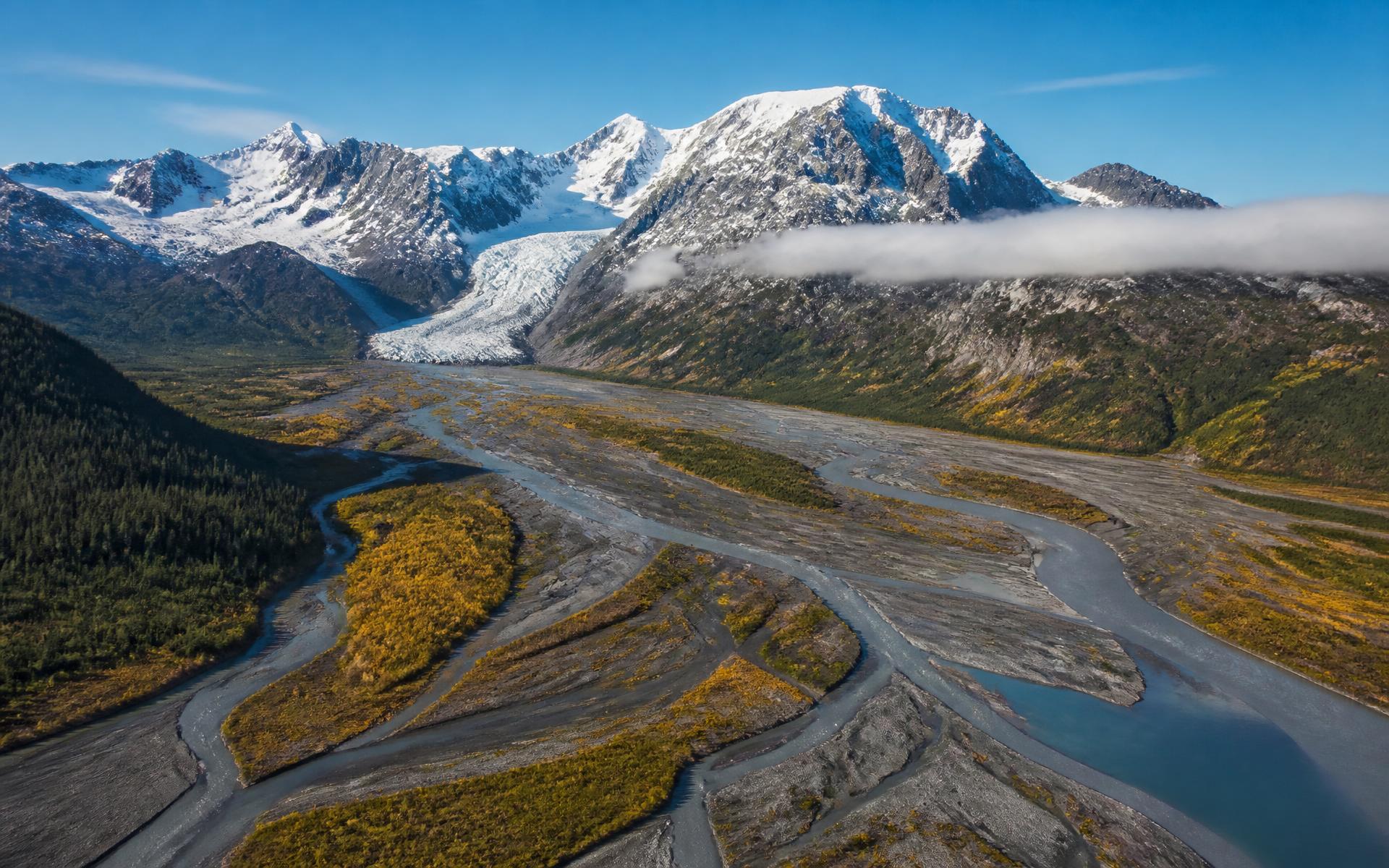 a braided glacial river valley below snow-capped peaks with a glacier tongue descending between the ridges at Alaska Inside Passage, United States, in morning light — original Triple VIP destination visual.